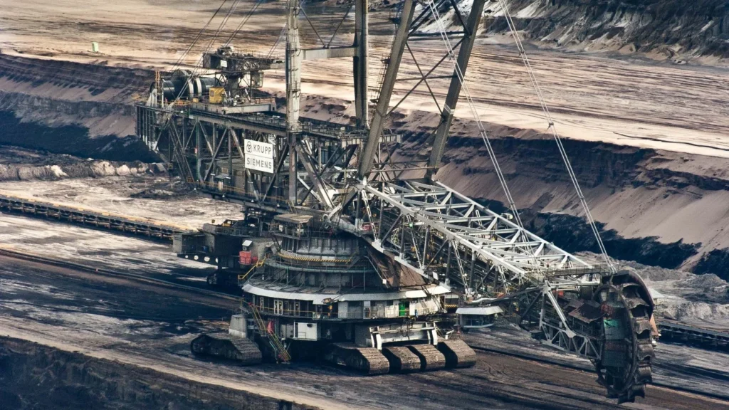 A large bucket-wheel excavator operating in an open-pit coal mine, showing industrial excavation machinery and earthmoving activity.
