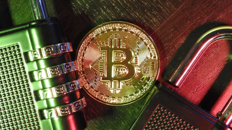 Koyu bir zemin üzerinde, bir adet fiziksel Bitcoin sembolü ve yanında şifreli bir asma kilit bulunan, kripto para güvenliğini ve dijital varlıkların korunmasını simgeleyen görsel.