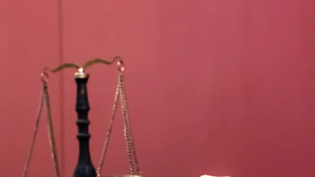 Kırmızı bir arka plan önünde duran, adaleti simgeleyen geleneksel bir hukuk terazisi.