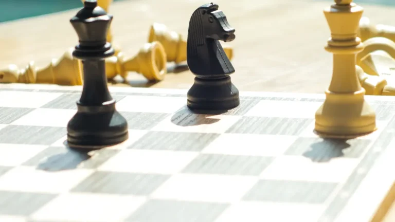 Satranç tahtası üzerinde devrilmiş beyaz taşlar ve ayakta duran siyah vezir, at ve beyaz şah figürlerini içeren, strateji ve rekabeti simgeleyen bir görsel.